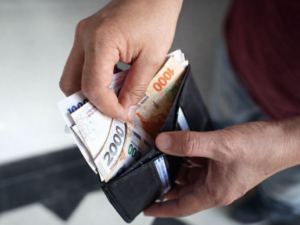 Manos de un jubilado contando billetes de una billetera por el aumento de la jubilación mínima en marzo 2026