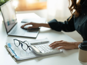 Mujer joven realizando cálculos con calculadora y laptop para revisar la recategorización de oficio ARCA en el portal oficial