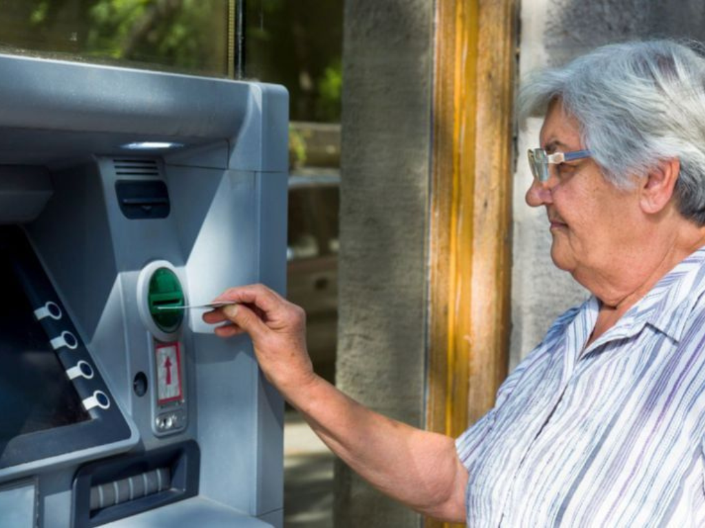 Jubilada consultando el calendario pagos ANSES en un cajero automático."