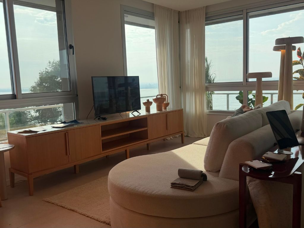 Interior del living con sofá curvo y vista panorámica al río en el departamento modelo de MiraRío San Lorenzo.